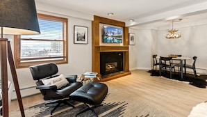 Een moderne woonkamer met een open haard, een wandgemonteerde televisie en een eethoek met een tafel en stoelen.