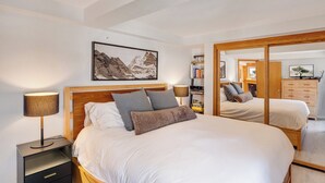 Een slaapkamer met een groot bed, nachtlampen, een boekenkast en een spiegel.