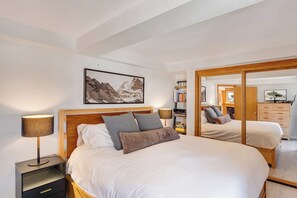 Un dormitorio con una cama grande, lámparas de noche, una estantería y un espejo.