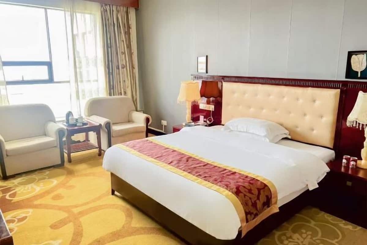A hotel room with a bed, a sofa, a small table, a nightstand, and a window with curtains.