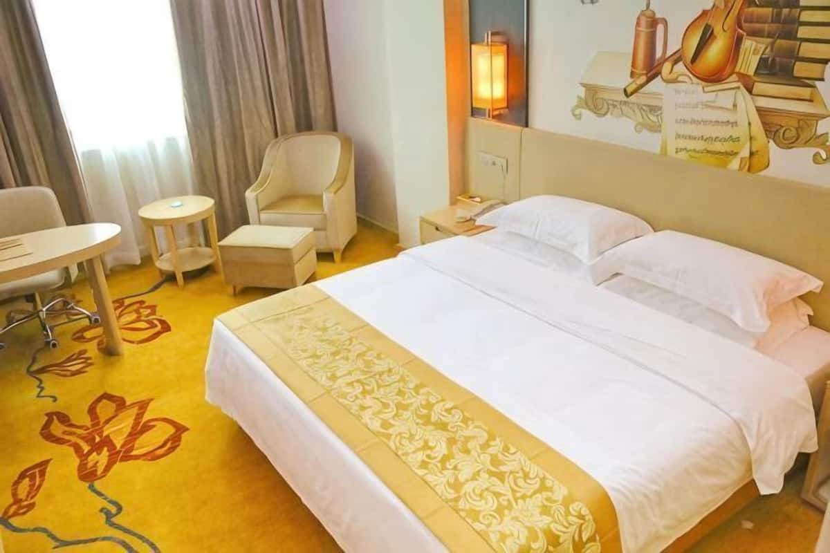 A hotel room with a large bed, a desk, a chair, and a small table.