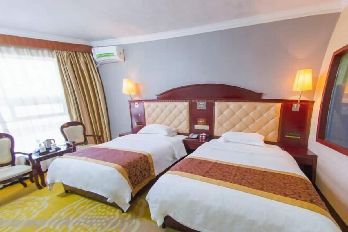 A hotel room with two beds, a desk with a chair, a lamp, and an air conditioning unit.