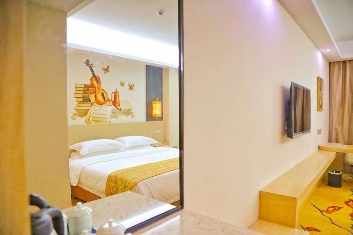 A hotel room with a bed, a TV, a mirror, and a small seating area.
