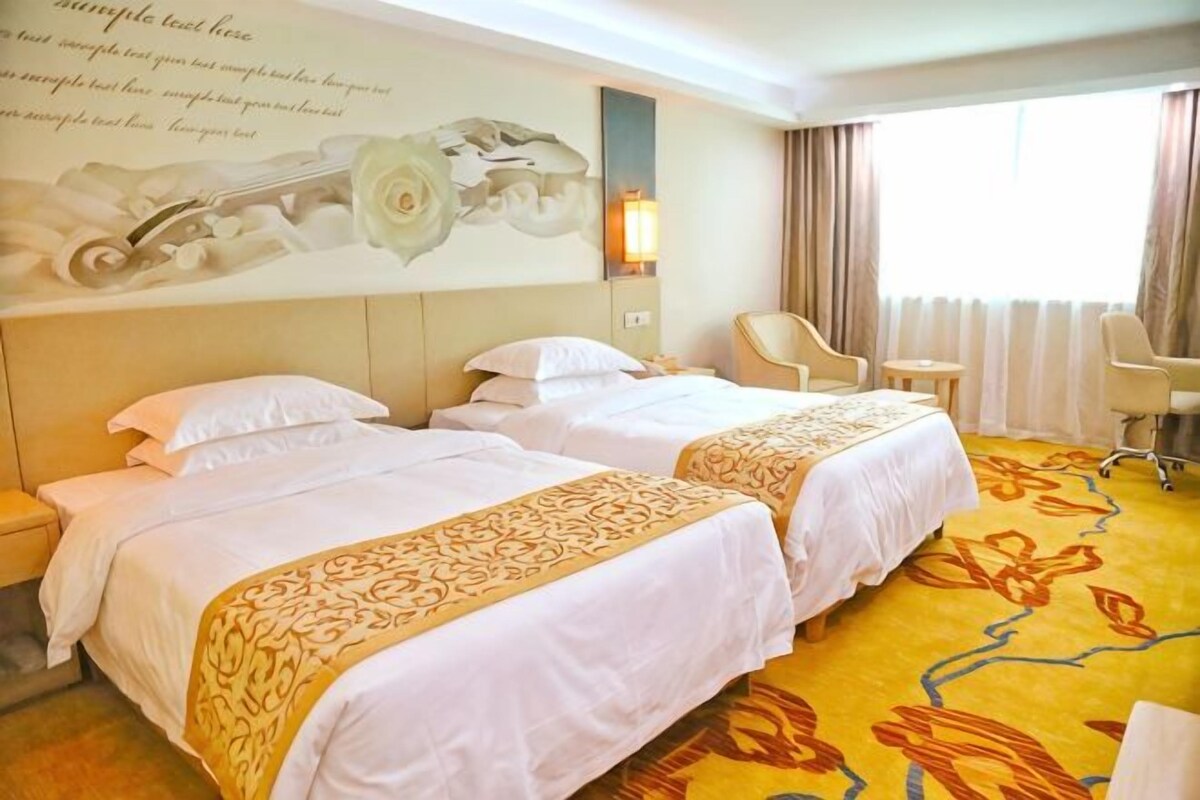 A hotel room with two beds, a chair, a desk, and a large window with curtains.