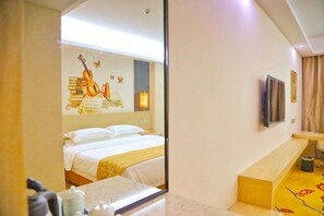 Quarto de hotel com cama, televisão, espelho e um pequeno espaço para sentar.