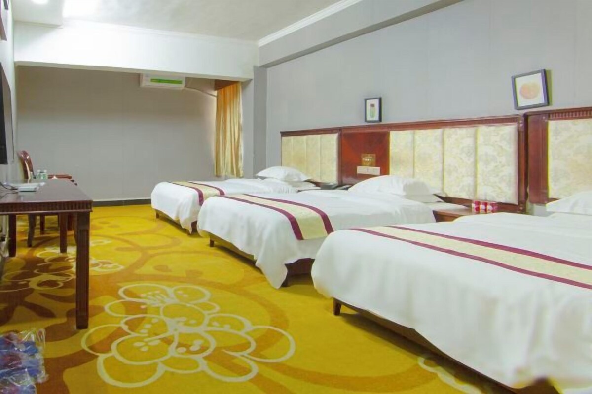 A hotel room with three beds, a wooden table, and a patterned carpet.