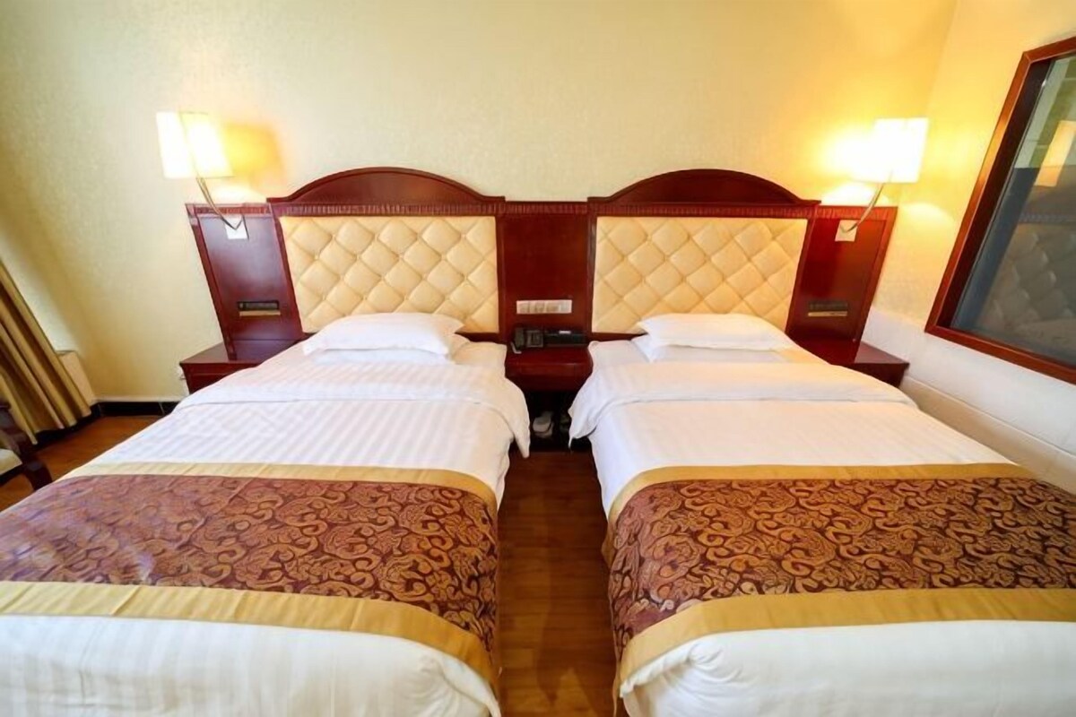 A hotel room with two beds, wooden headboards, bedside tables, lamps, and a window.