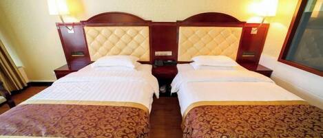 Quarto de hotel com duas camas, cada uma com cabeceira, mesas de cabeceira, abajures e um criado-mudo pequeno.
