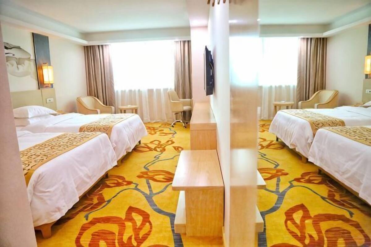 A hotel room with two beds, a desk, a chair, and a TV.
