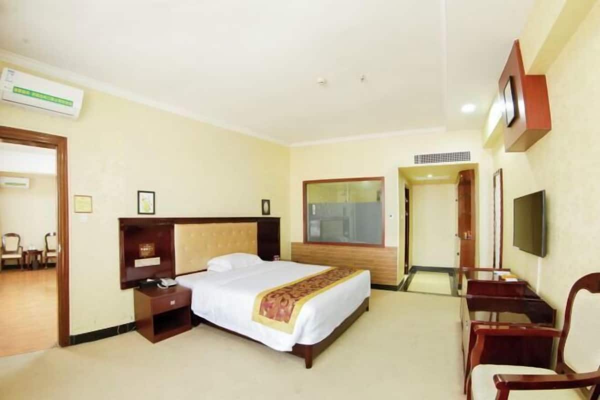 A hotel room with a bed, bedside table, TV, and a desk with chairs.