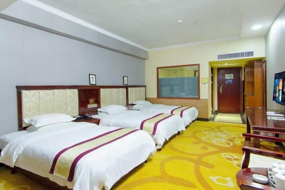 A hotel room with three beds, a television, a desk, and a chair.