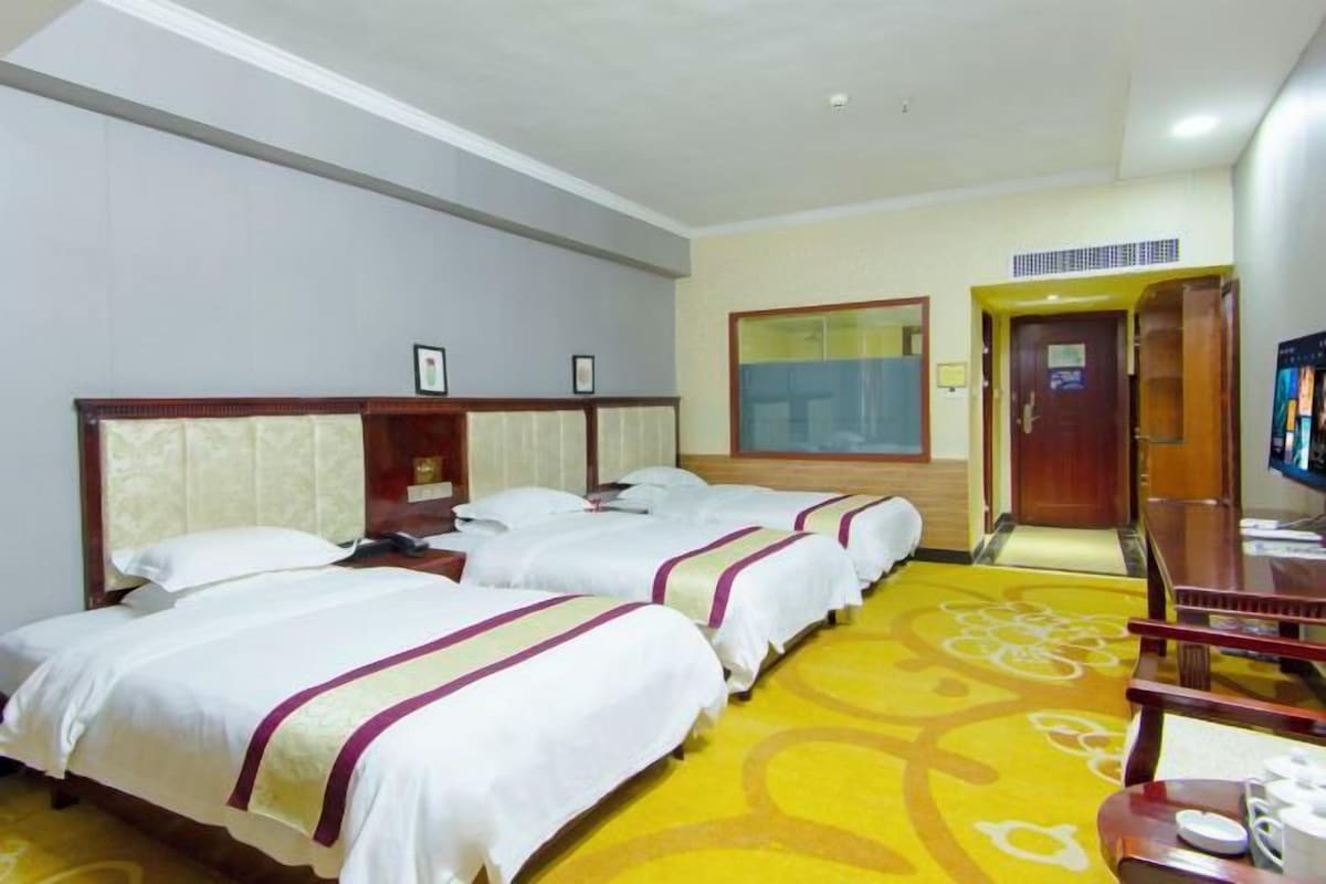 A hotel room with three beds, a television, a desk, and a chair.