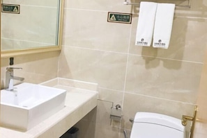 A bathroom with a white sink, a mirror, and a toilet. There are signs indicating a wet floor and a small area. - Bobai Baolilai Hotel (Bobai)