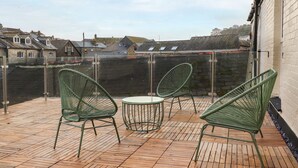 Een houten terras met groene stoelen en een tafel, met uitzicht op een stadsbeeld met gebouwen en een waterpartij.