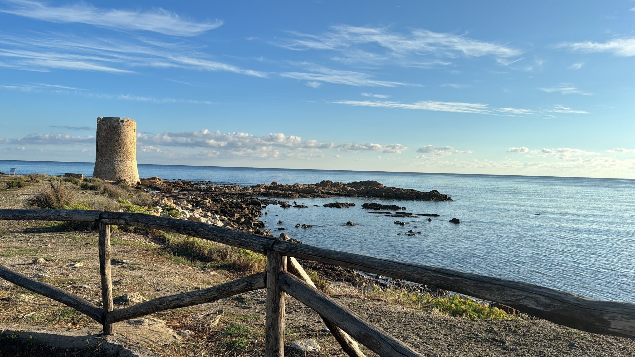 A coastal landscape with a stone tower, rocky shoreline, and calm sea.