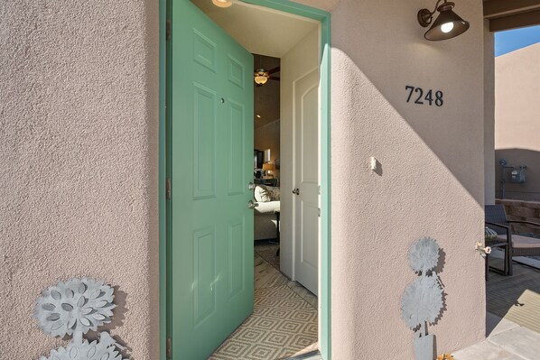 A hallway with a green door leading to a room, a number '7248' on the wall, and a decorative metal piece on the floor.