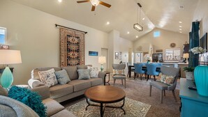 A spacious living room with a large sofa, a coffee table, and a dining area with blue chairs. - Luxurious Open Concept Home with Fabulous Backyard Entertainment Area (Santa Fe)