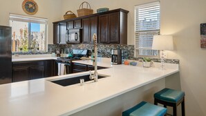 A modern kitchen with dark wood cabinets, a stainless steel refrigerator, a built-in oven, and a large island with a sink. - Luxurious Open Concept Home with Fabulous Backyard Entertainment Area (Santa Fe)