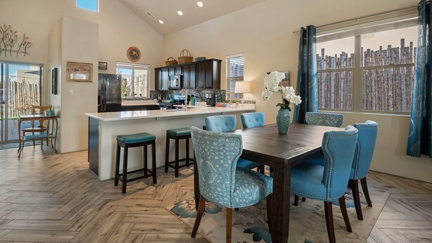 A modern kitchen with dark cabinets, a central island, and a dining area with blue chairs. - Luxurious Open Concept Home with Fabulous Backyard Entertainment Area (Santa Fe)