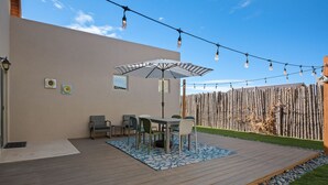 A wooden deck with a table and chairs, a striped umbrella, and a string of lights against a clear sky. - Luxurious Open Concept Home with Fabulous Backyard Entertainment Area (Santa Fe)