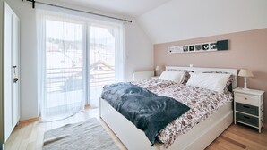 Un dormitorio con cama, mesita de noche, ventana con cortinas y vista a edificios.