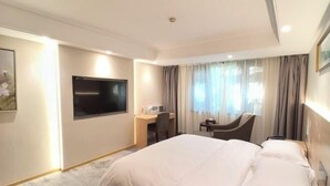 Een hotelkamer met een bed, een bureau, een stoel, een televisie en een raam met gordijnen.