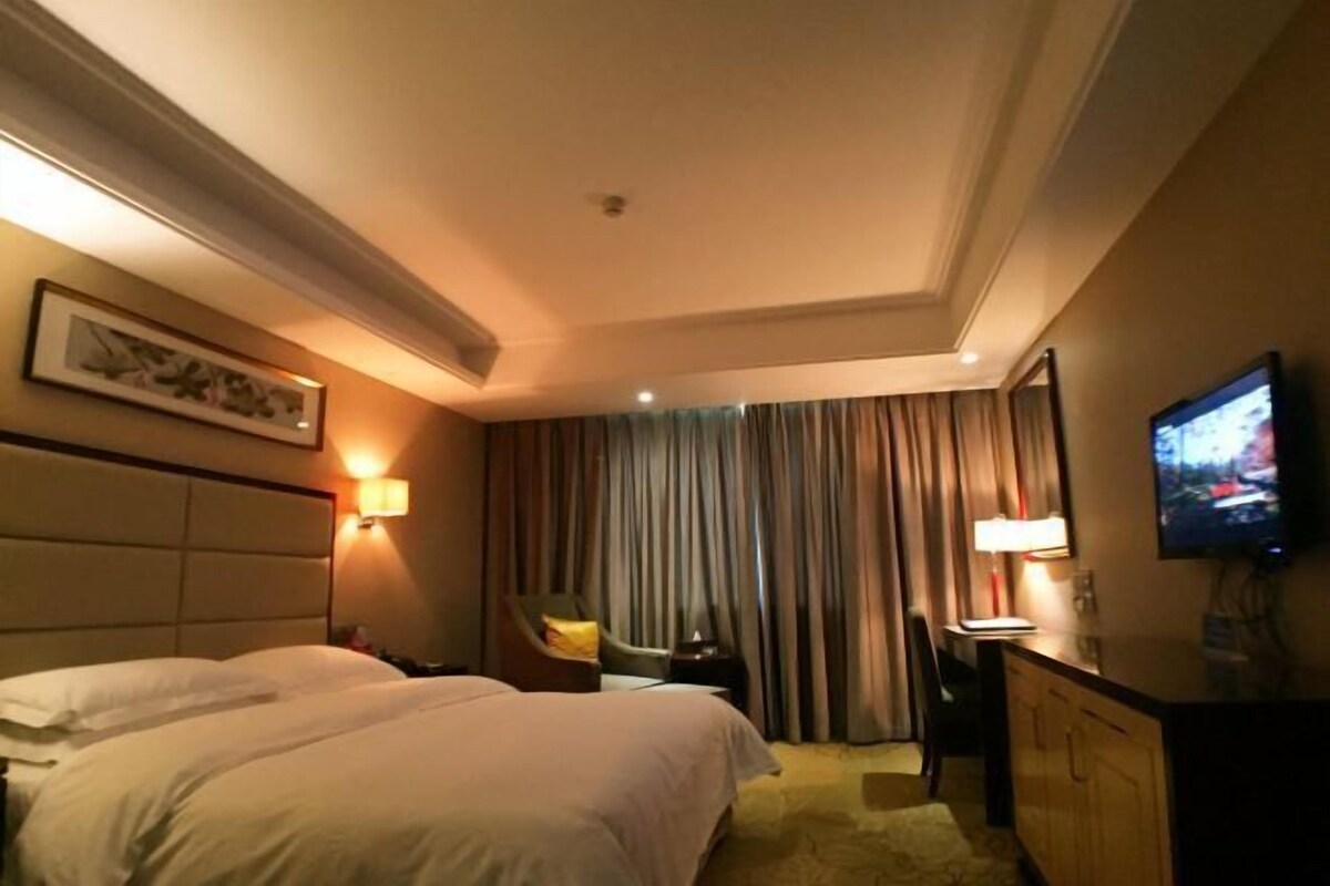 A hotel room with a large bed, a desk, a chair, a television, and a window with curtains.