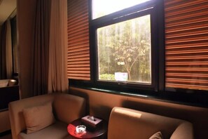 A room with a sofa and armchairs, a small table with a tissue box and a glass, and a window with blinds. - Lianhua Hotel (Xiangcheng)
