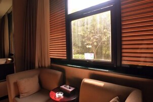 A room with a sofa and armchairs, a small table with a tissue box and a glass, and a window with blinds.