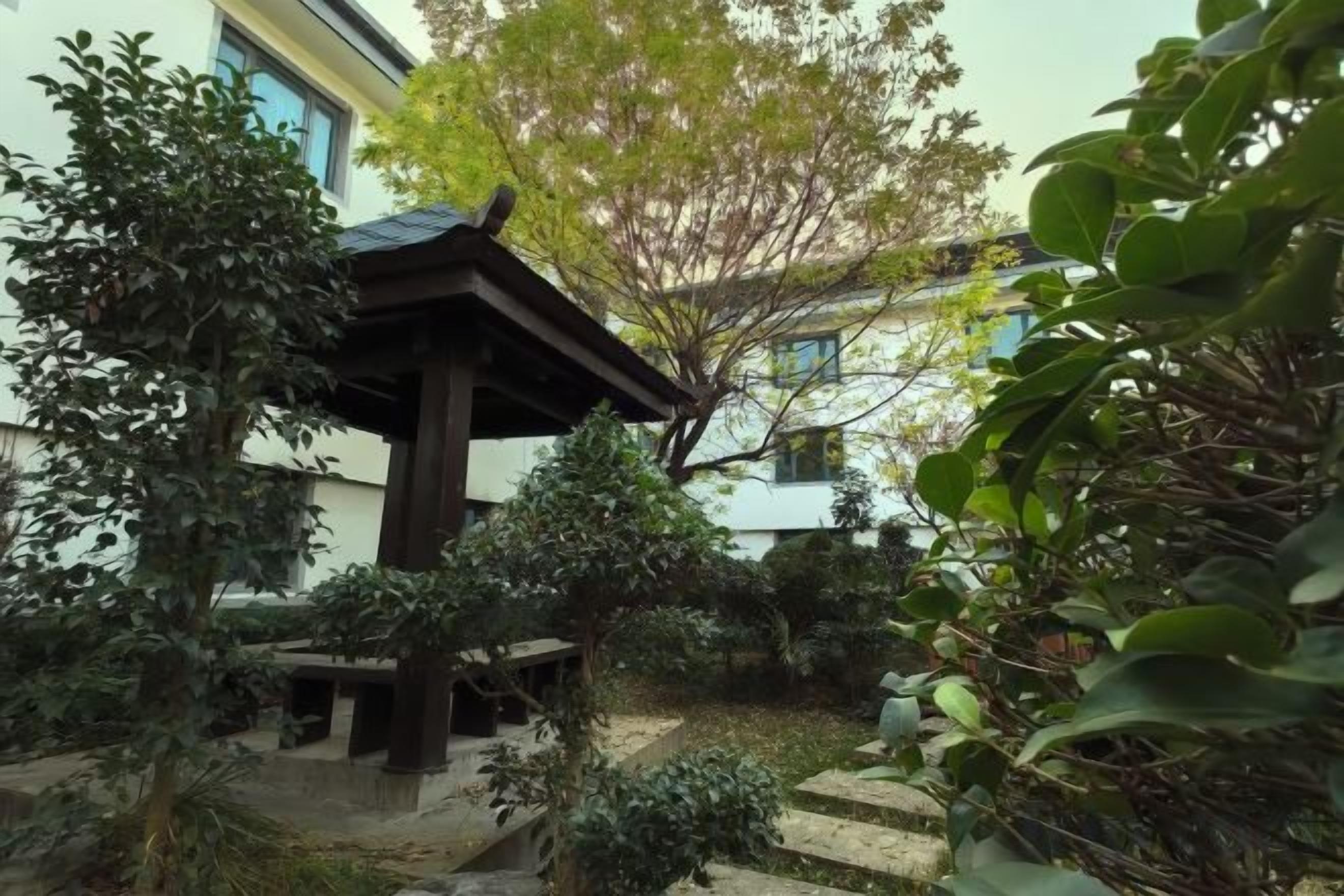 A traditional Japanese-style garden with a wooden gazebo, stone pathways, and various plants.