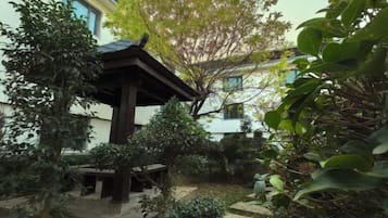 A traditional Japanese-style garden with a wooden gazebo, stone pathways, and various plants.
