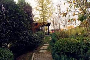 Un vialetto in giardino conduce a un gazebo, immerso in vegetazione lussureggiante e circondato da un muro in mattoni.