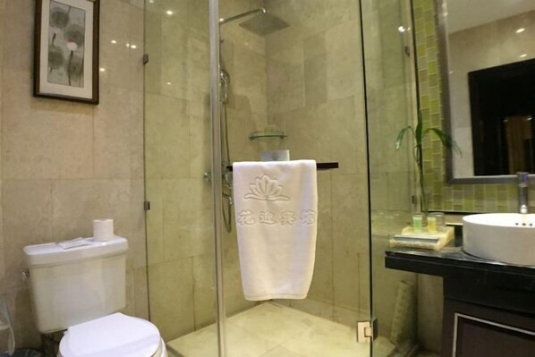 A glass-enclosed shower stall with a white towel hanging on the door, a toilet, and a sink with a mirror above it. - Lianhua Hotel (Xiangcheng)