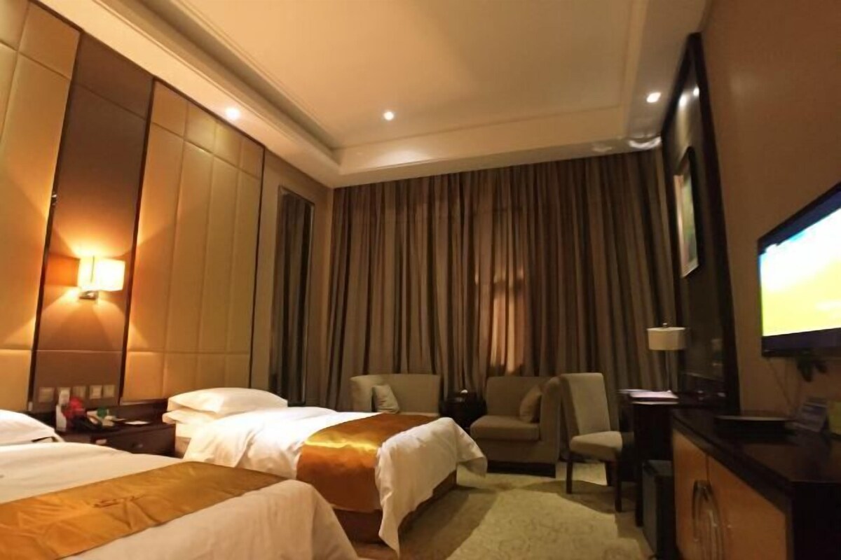 A hotel room with two beds, a desk, a chair, a television, and a large window with curtains.