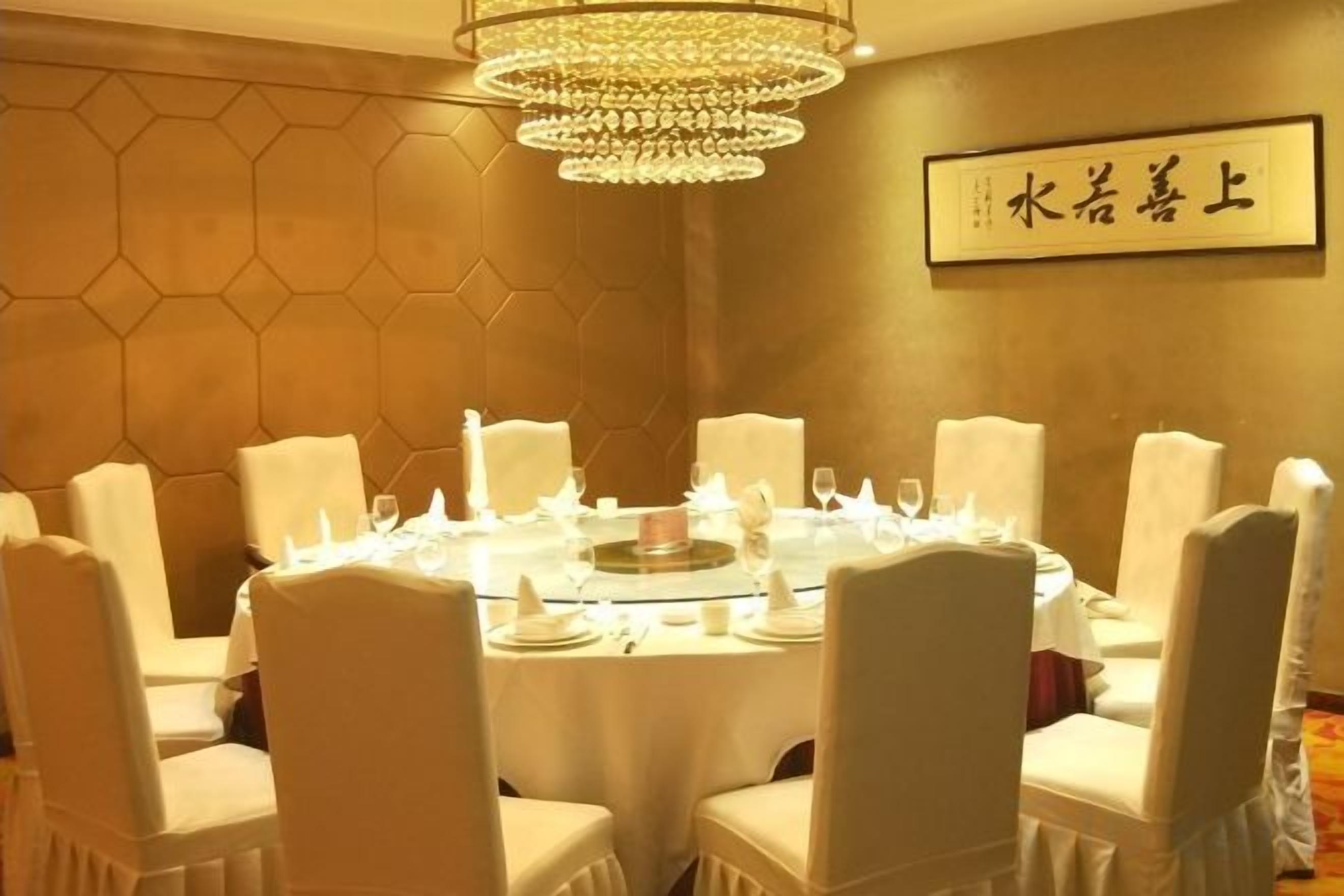 Un comedor con una mesa redonda dispuesta para ocho personas, rodeada de sillas, y un candelabro colgando sobre ella.