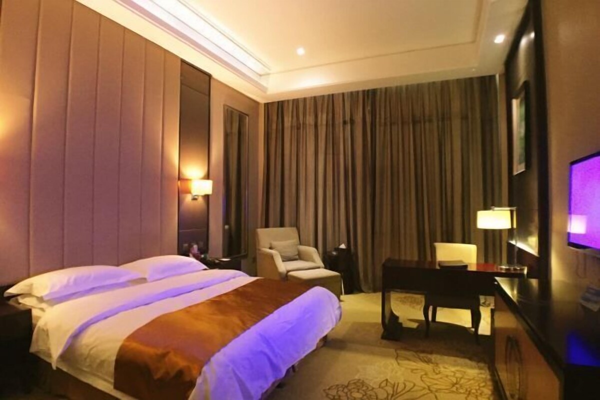 A hotel room with a bed, a chair, a desk, and a TV.