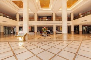 Eine geräumige Lobby mit gefliestem Boden, mehreren Ebenen und einem zentralen Zierbereich.