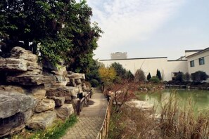 A pathway beside a rock wall leading to a building with a pond. - Lianhua Hotel (Xiangcheng)