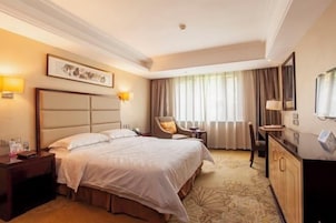 A hotel room with a large bed, a desk, a chair, and a television.