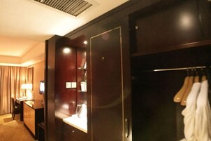 A hotel room with a wooden wardrobe, a desk with a lamp, and a mirror.