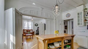 Een ruime keuken met witte kasten, een houten eiland met pannen en keukengerei, en een kroonluchter.