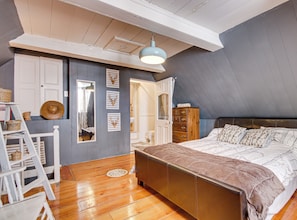 A bedroom with a wooden floor, a bed with a patterned bedspread, a dresser, and a ladder.
