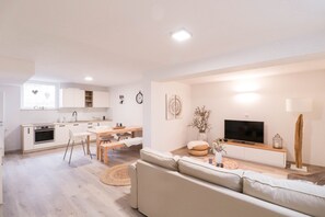 A modern living room with a sofa, TV, and a dining area with a table and chairs. - Cozy apartment Below Eden (Bled)