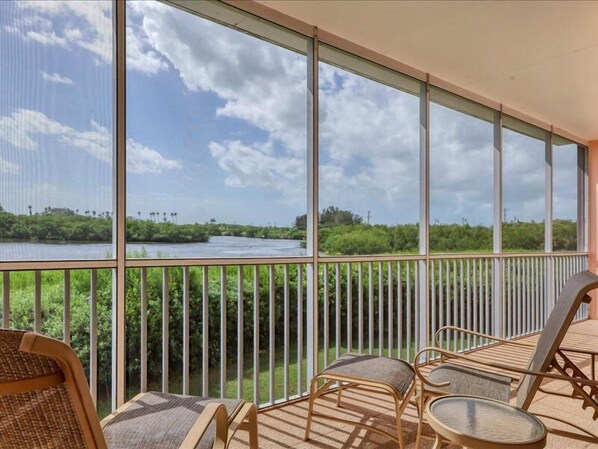 A balcony with a view of a river and greenery, furnished with wicker chairs and a small table.