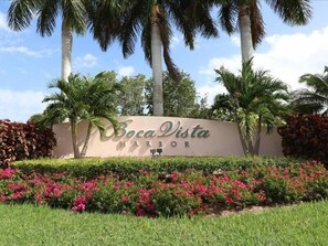 A sign for Boca Vista Harbor with a landscaped foreground featuring pink flowers and palm trees.