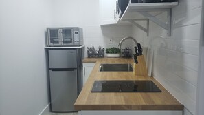 A compact kitchen with a built-in microwave, a refrigerator, a sink, and a wooden countertop.