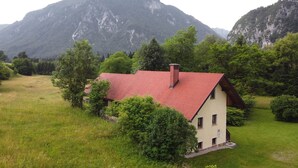 A house with a red roof, surrounded by lush greenery and mountains in the background. - House Alpine Rose - Apartment Toni (Mojstrana)