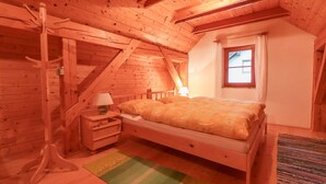 A wooden room with a bed, a nightstand, a lamp, a window, and a wooden coat rack. - House Alpine Rose - Apartment Toni (Mojstrana)
