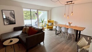 A modern living room with a sofa, a dining table with chairs, and a large window.