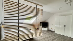 A modern living room with a slatted partition, a wooden floor, a white wardrobe, and a ceiling fan.